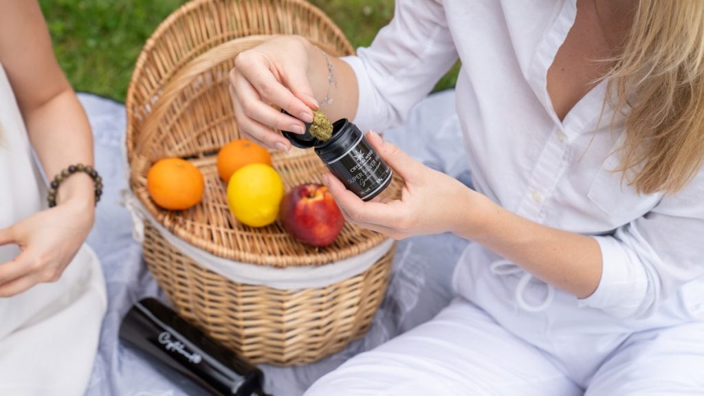two women sitting on the grass with a basket of fruit
