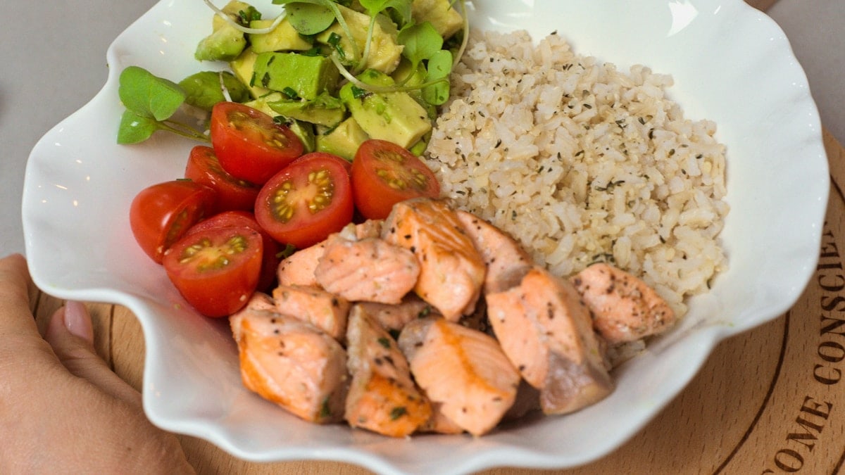 a white bowl filled with chicken, rice, tomatoes and avocado